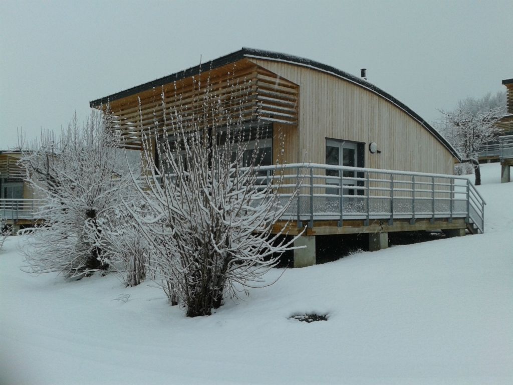 Camping Auvergne : Les chalets en hiver sous la neige, avec vue sur un volcan et un lac naturel.